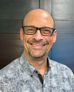 A middle-aged bald man wearing glasses and a broad smile.